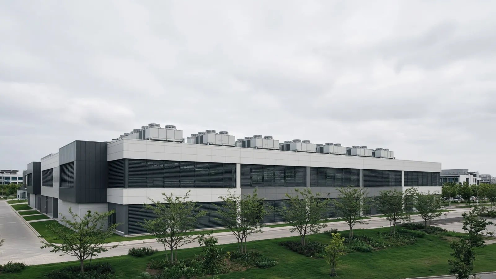 A low rise data centre building with rooftop cooling plant, set in landscaped grounds on an overcast day